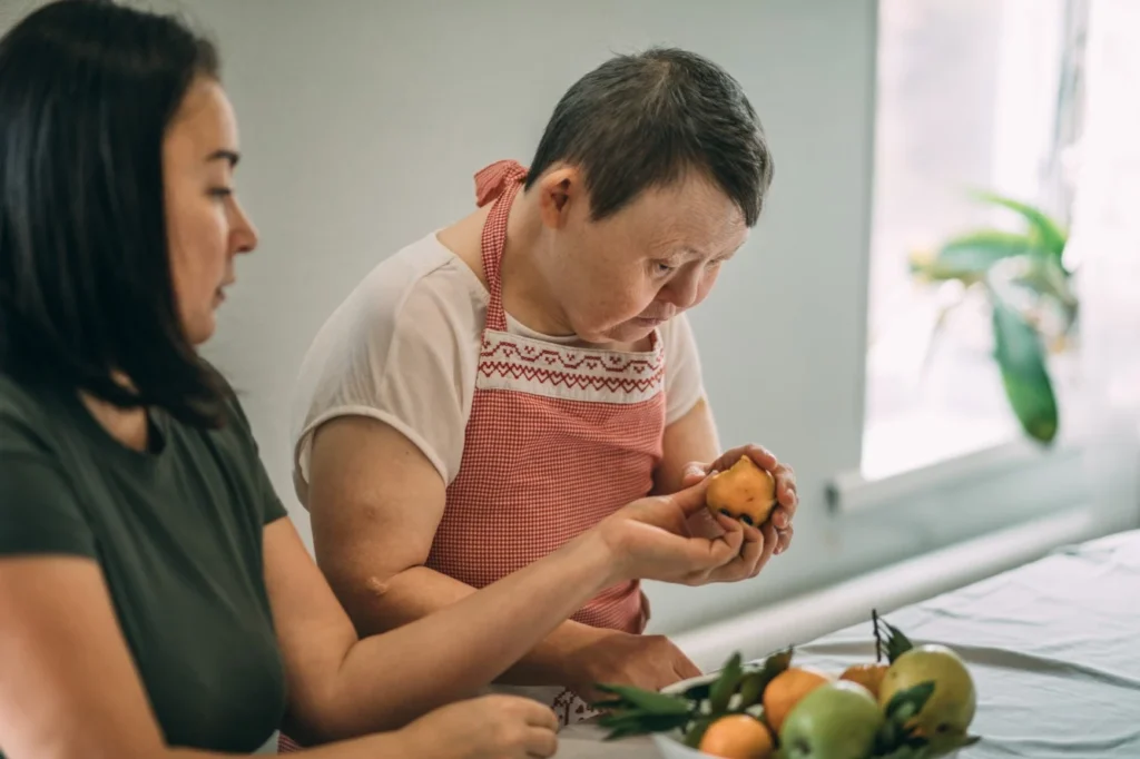 Woman with down syndrome organising fruit at home with carer