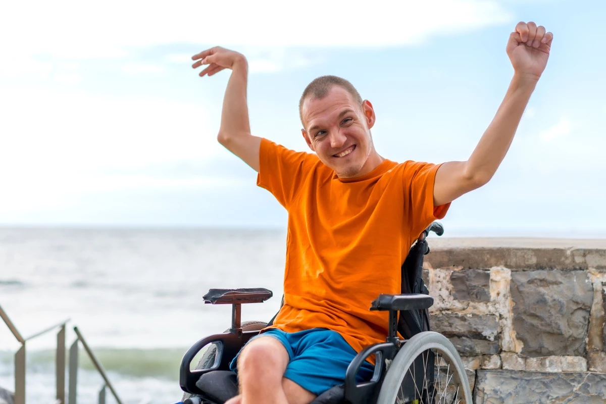 Happy disabled man in wheelchair smiling and lifting arms in the air